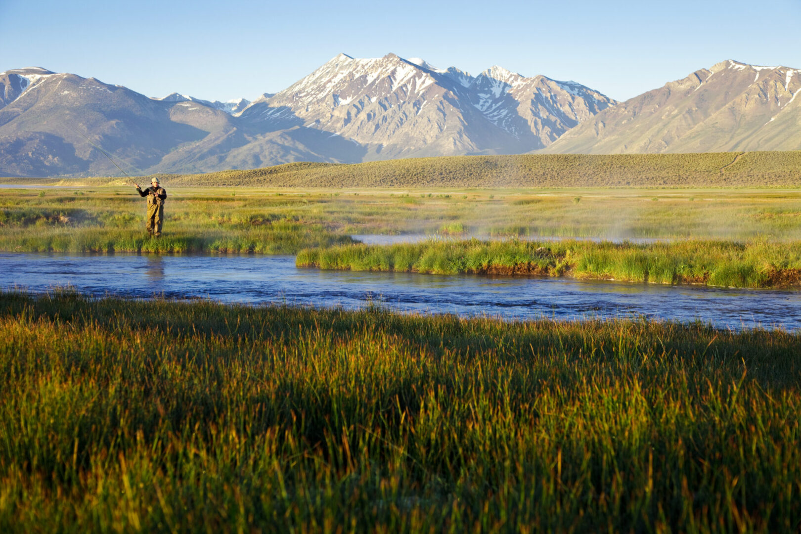 One man fly fishing on the Owens River at sunrise with the Sierra Nevada Mountains in the distance